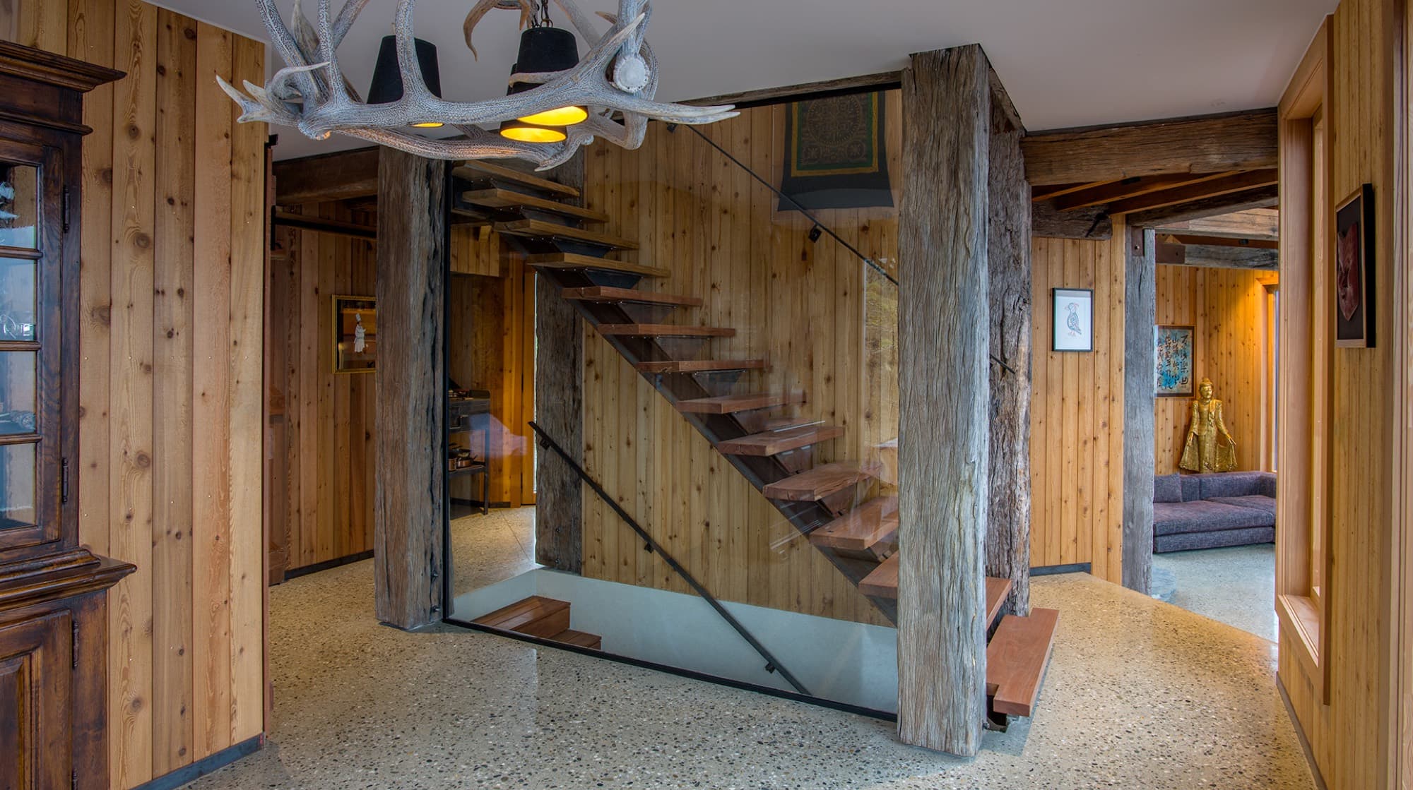 The entry hall with terrazzo floor, recycled timber posts, an antler chandelier and hardwood stairs rising to the upper floor