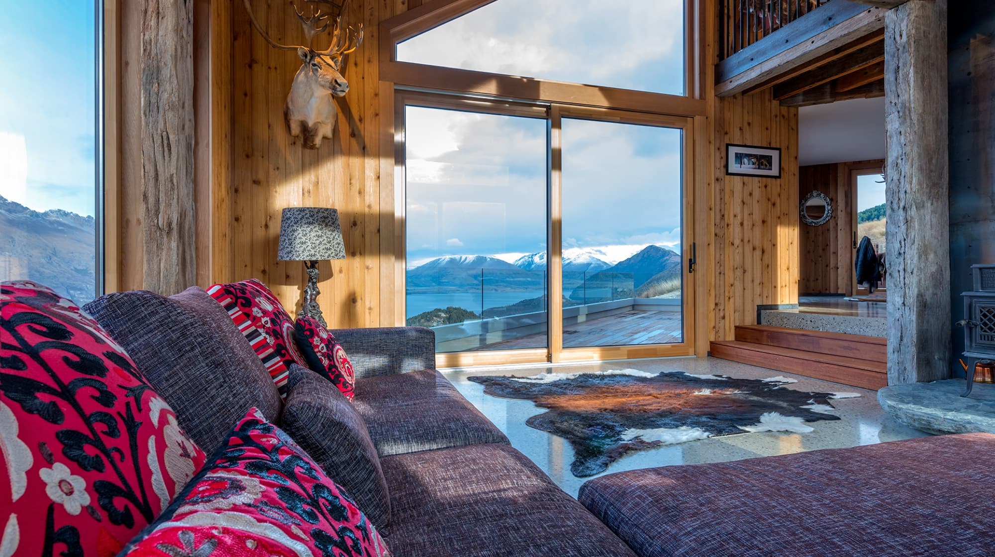 The living room with cedar walls, recycled ironwood beams and full-height glass onto Lake Wakatipu and the mountains