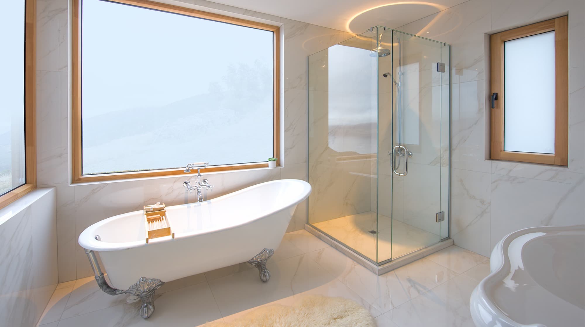 The white marble ensuite with a clawfoot bath beneath a picture window and a glass rainfall shower
