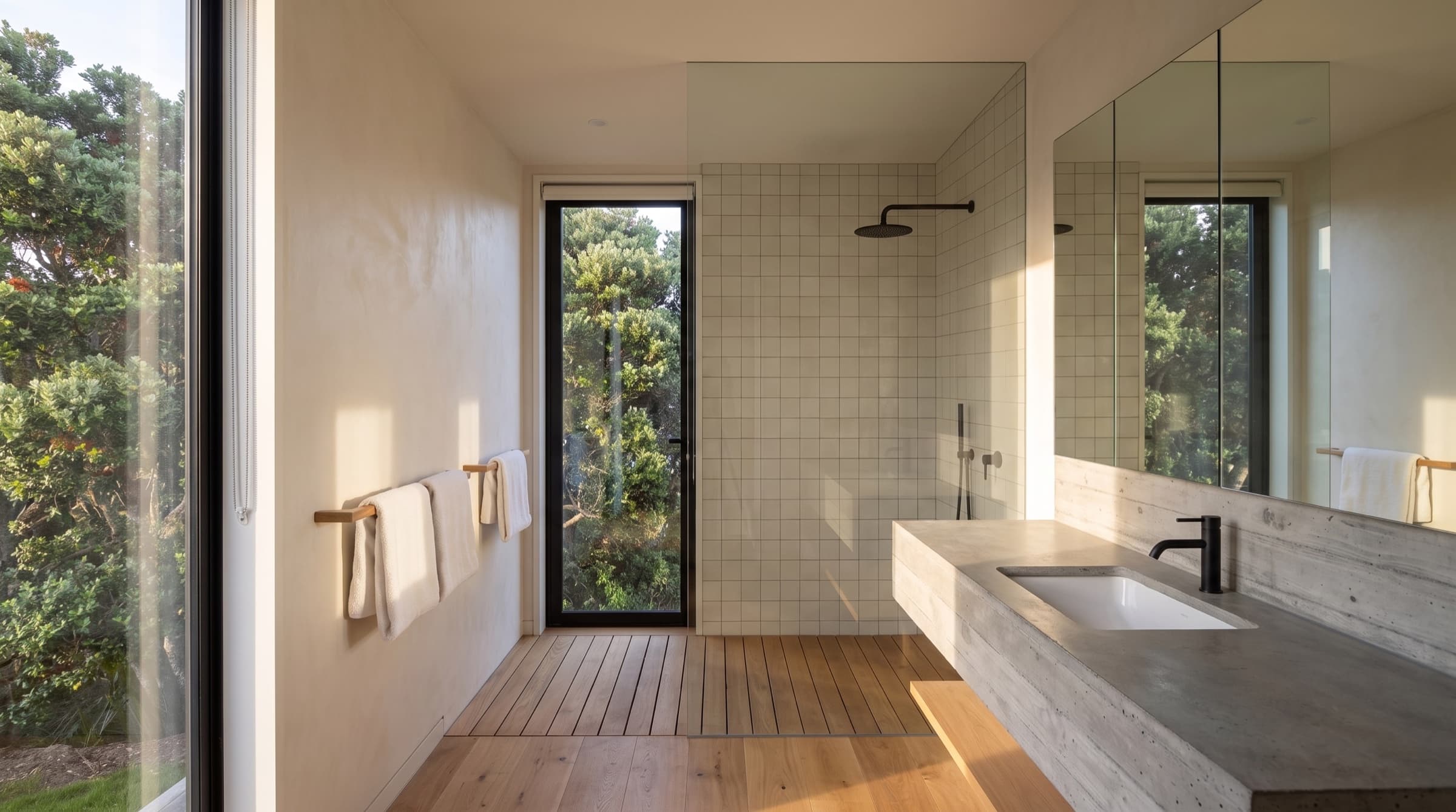 The main bathroom, a board-formed concrete vanity and walk-in shower with a narrow window onto the pōhutukawa