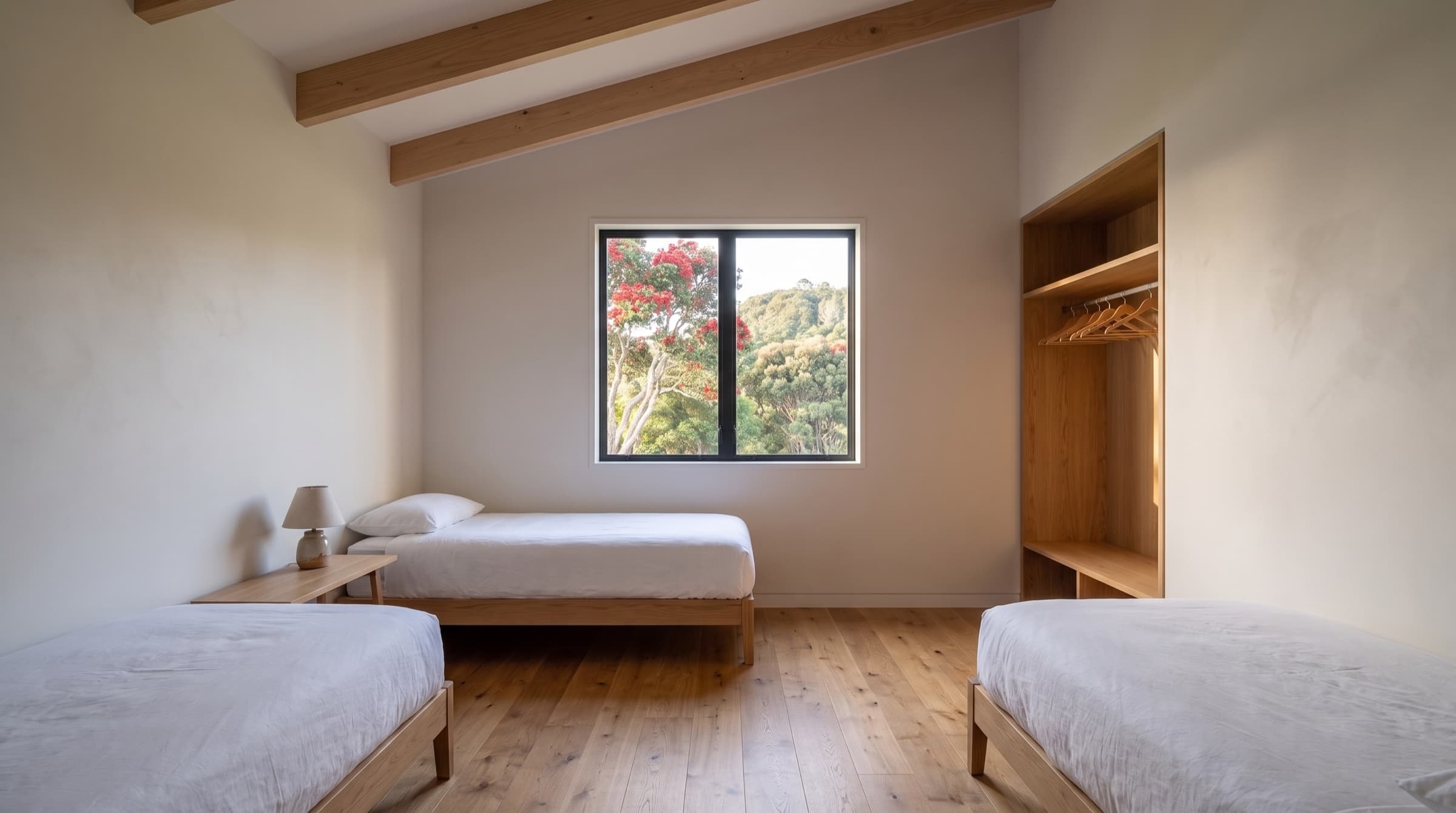 The twin room, two low oak beds in white linen with a window onto the pōhutukawa and the bush hill