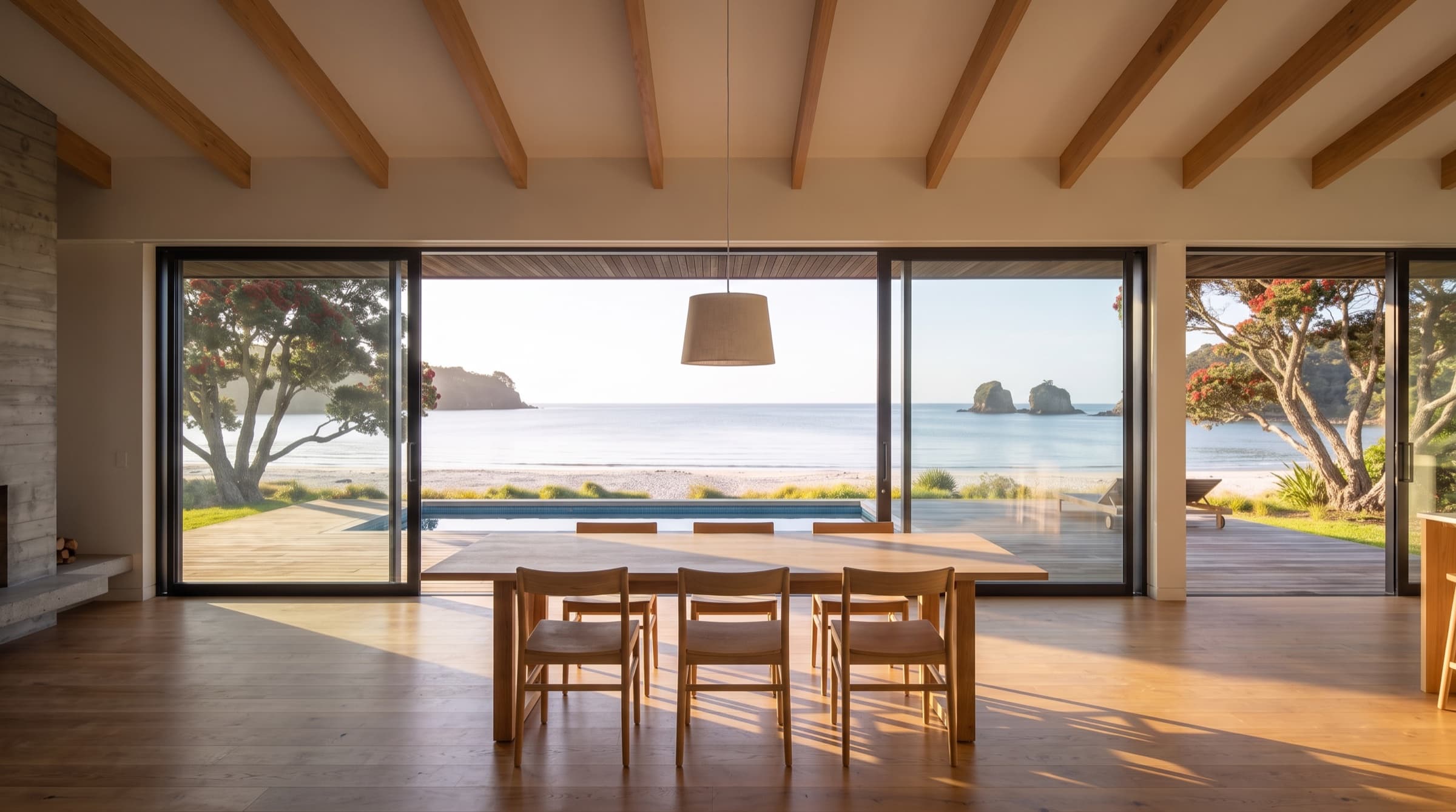 The oak dining table beside full-height sliders standing open onto the deck and the bay