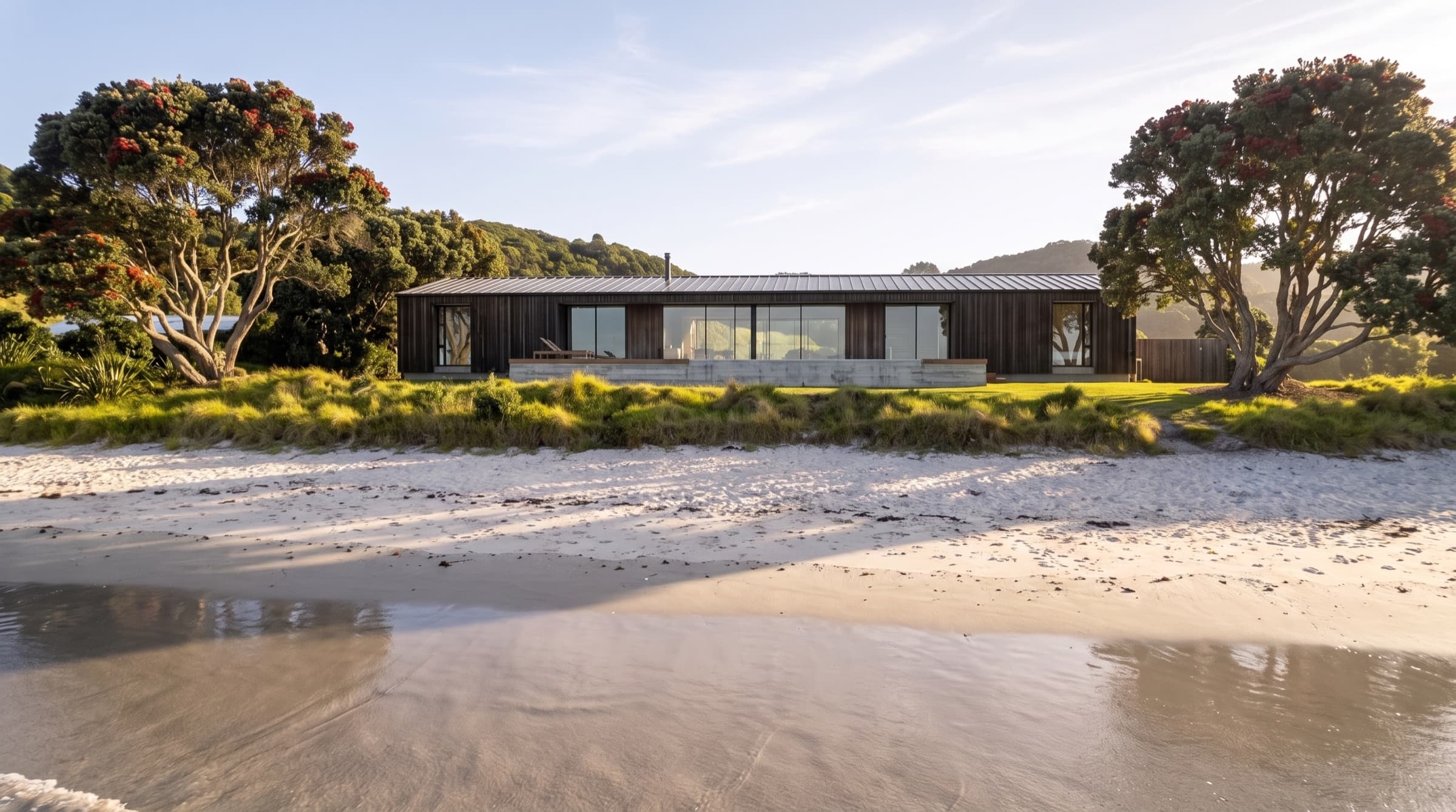 Tideline House seen from the beach at dawn, long and low on its grassed terrace above the sand