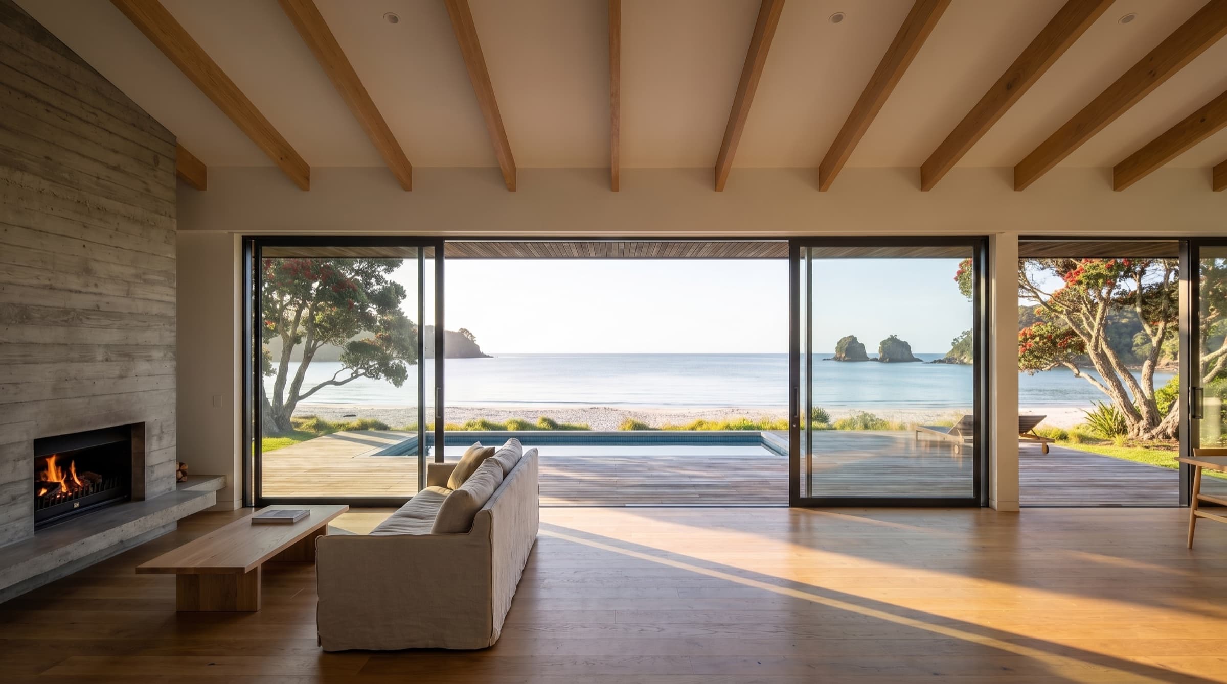 The living room looking out through open full-height sliders to the pool, the beach and Mercury Bay
